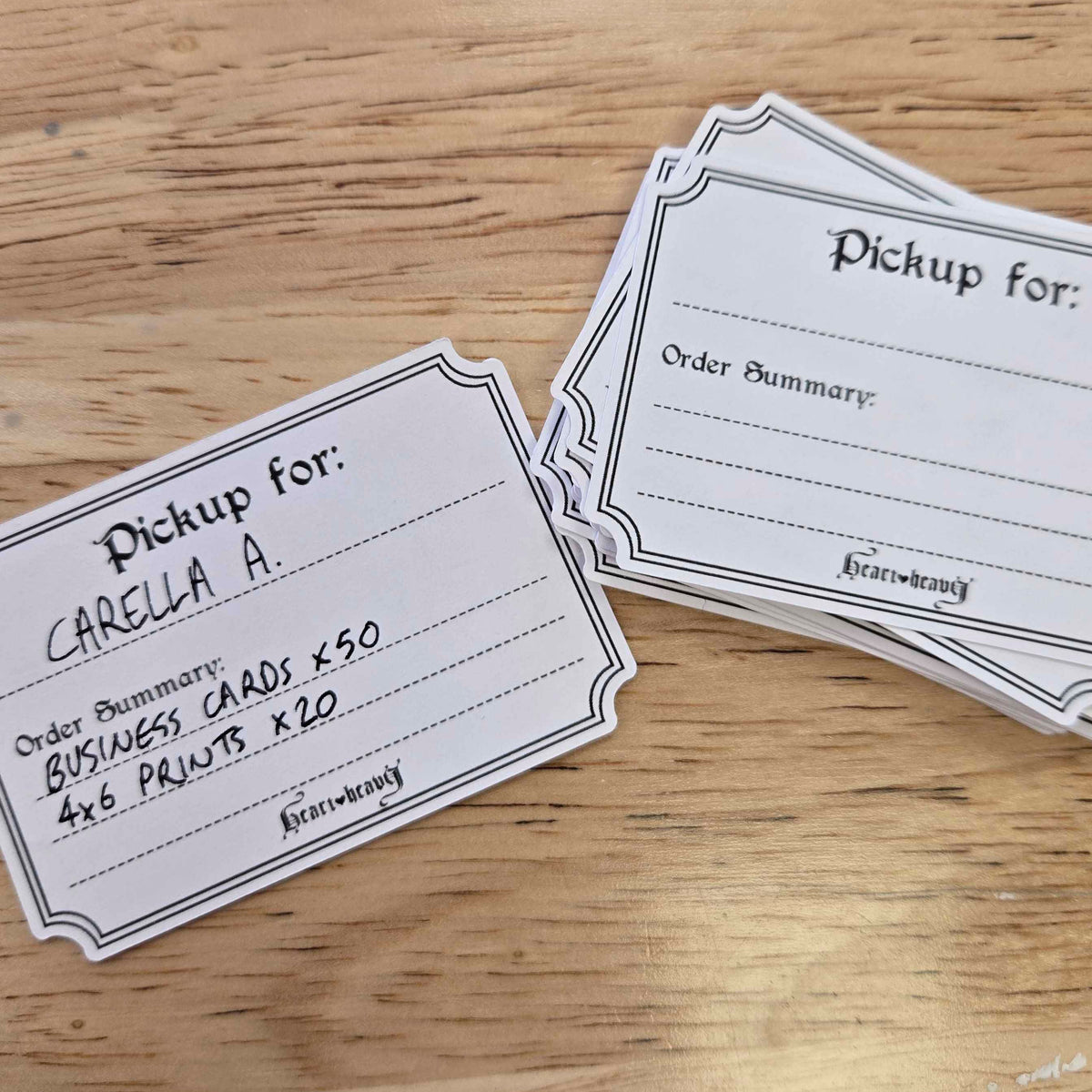 A stack of white paper pickup cards with black printed text and borders, placed on a light wood tabletop. One card is laid flat in front, and a second stack sits behind it.