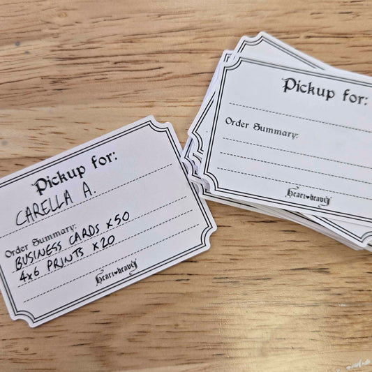 A stack of white paper pickup cards with black printed text and borders, placed on a light wood tabletop. One card is laid flat in front, and a second stack sits behind it.